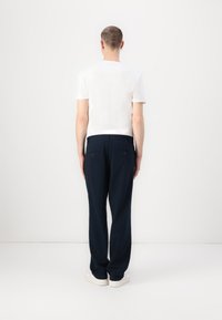 White short-sleeve t-shirt paired with navy trousers. Trousers feature rear pockets and a straight-leg design, with minimal texture details.