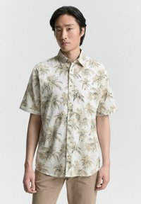 Chemise à manches courtes en tissu beige clair avec un motif de palmier en brun foncé. Fermeture à boutons avec un col classique et coupe décontractée.