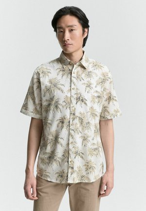 Chemise à manches courtes en tissu beige clair avec un motif de palmier en brun foncé. Fermeture à boutons avec un col classique et coupe décontractée.