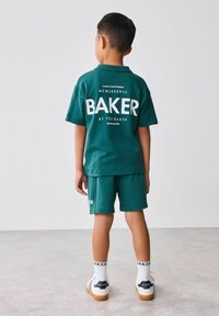 Zelený bavlnený polo a šortky s bielym nápisom "BAKER". Skombinované s bielymi ponožkami s nápisom "BAKER" a bielymi topánkami s námorníckymi akcentmi.