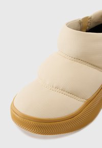 Zapato sin cordones acolchado en color beis con suela de goma, tejido texturizado y punta redonda. La suela presenta un patrón de espiga para mayor tracción.