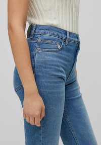 Modré džíny s vysokým pasem a slim fit, které mají klasickou denimovou texturu, jemné švy a logo na zadním pásku.
