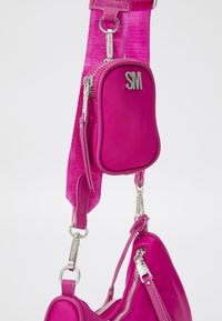 Borsa a tracolla rosa con tracolla testurizzata, dotata di tasca con zip e hardware argentato. Superficie liscia con dettaglio del logo sulla parte superiore.