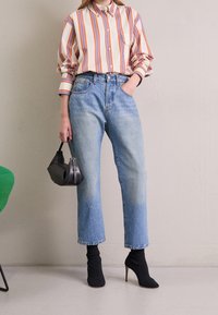 Randig skjorta i krämfärgad, orange och blå; ljusblå högmidjade jeans; svart handväska; svarta strumpstövlar; texturerade ytor.