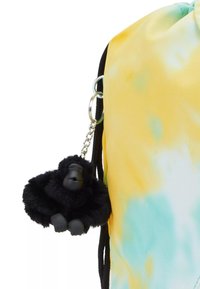 Sac à dos à cordon avec un motif tie-dye jaune et turquoise. Il possède un porte-clés en peluche représentant un gorille noir attaché pour plus d'embellissement.