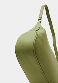 Grøn skuldertaske i imiteret læder med en glat overflade, buet form og guldhardwaredetaljer. Præget logo på siden.