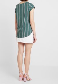 Grönrandig topp med korta ärmar och böjd nederkant, ihop med en vit kjol och rosa klacksandaler.