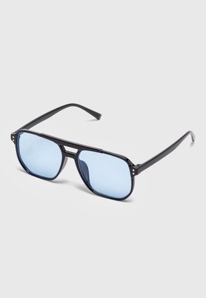 Occhiali da sole stile aviatore neri con montature sottili e lenti leggermente azzurre su sfondo grigio.