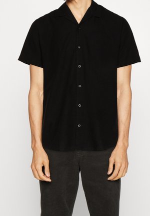 Chemise noire à manches courtes en tissu doux, avec un design à col et six boutons noirs sur le devant. Texture lisse, coupe décontractée.