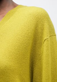 Sweter w serek w jaskrawym żółtym kolorze, z teksturowanym splotem, w oversize'owym kroju oraz prążkowanymi detalami wzdłuż dekoltu i dołu.