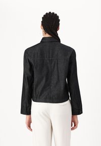 Chaqueta de mezclilla negra con un ajuste entallado, mangas largas y cuello clásico de botones. Costuras visibles y bolsillos en la parte trasera.