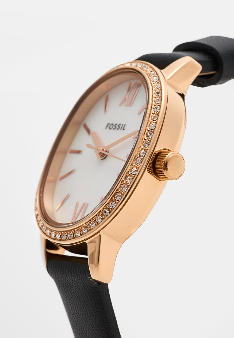 Roze gouden horloge met een witte wijzerplaat, Romeinse cijfers, kristalaccenten rondom de bezel en een zwarte leren band.