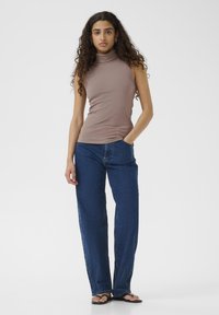 Top smanicato a collo alto marrone a coste abbinato a jeans blu a gamba dritta e infradito nere. Design semplice, vestibilità su misura.