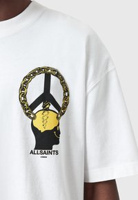 Hvid bomulds t-shirt med en sort og gul grafik af et hoved med en kæde og fredssymbol, samt teksten "ALLSAINTS LONDON".