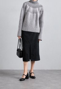 Harmaa ribbineuleinen poolopaita, musta polvipituinen hame halkiolla ja mustat paksukorkoiset kengät. Pieni musta käsilaukku täydentää asun.