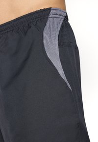 Close-up van zwarte sportshorts met elastische tailleband en contrasterende grijze meshpanelen in het gebied van de zijzakken.