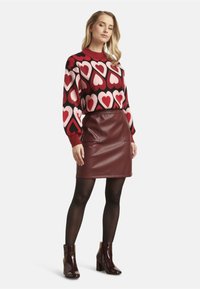 Knit sweater with red and pink heart pattern, paired with a burgundy leather skirt, black tights, and glossy ankle boots.