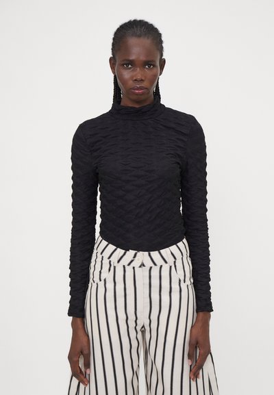 Black cropped long-sleeve top with textured fabric featuring a high neck, paired with high-waisted beige and black striped wide-leg pants.