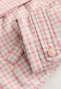 Tissu à carreaux vichy rose et blanc avec un pli et un détail de bouton unique, présentant une texture lisse et des coutures contrastantes.