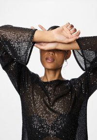 Top preto transparente com mangas sino largas, decorado com lantejoulas, apresentando um decote redondo e um acabamento texturizado.