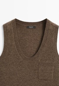 Brun stickad ärmlös topp med en djup V-halsringning, med en liten bröstficka. Mjuk textur och ett subtilt mönster. Märke synligt.