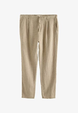 Beige linnen broek met een achterzak die is vastgemaakt met een enkele bruine knoop, gedragen met een donkergroen overhemd dat is ingestopt.