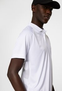 White polo shirt with a smooth texture, featuring a breathable mesh panel on the side. Completed with a collar and short sleeves.