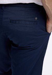 Pantaloni blu navy realizzati in tessuto morbido, con una tasca posteriore e un sottile dettaglio del logo del marchio. Design semplice con vestibilità su misura.