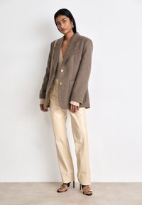 Brun uldblanding oversized blazer med guldknapper, parret med crèmerfarvede læderbukser med lige ben og sorte og brune hæle.