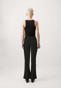 Black sleeveless top paired with high-waisted, flared dark green pants featuring back pockets and button details. Smooth texture, tailored fit.
