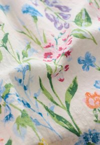 Cvetni material z belo podlago in barvitimi motivi modrih, roza, vijoličnih in zelenih cvetov. Mehka, teksturirana tkanina z podrobnimi vzorci.