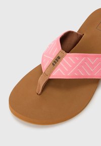 Roze flip-flop sandaal met een gestructureerde band met een visgraatpatroon, een gepolsterde teenpost en een bruine voetbed.