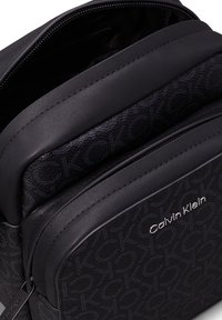 Zaino nero Calvin Klein con esterno testurizzato, multiple tasche con zip e materiale sintetico liscio con accento del logo.