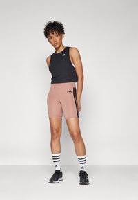 Débardeur noir court et shorts taille haute rose pâle avec des rayures noires sur les côtés. Chaussures de sport noires et chaussettes blanches avec des rayures noires.