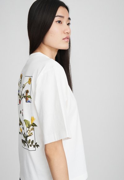 T-shirt en coton blanc à manches courtes, avec un imprimé floral au dos en jaune et vert. Forme simple, coupe décontractée.
