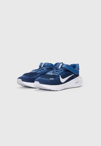 Zapatillas de punto azules con suela blanca, que cuentan con una correa segura y parte superior texturizada. Logotipo Swoosh blanco notable en el lateral.