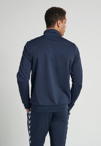 Marineblauwe sportieve lange mouwen jacket met hoge kraag, een gladde textuur en contrasterende zijstrepen. Geschikt voor sport en casual kleding.