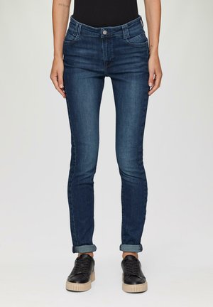 Dunkelblaue Denim-Skinny-Jeans mit fünf Taschen, leichter Used-Optik und hochgekrempelten Säumen, kombiniert mit schwarzen Sneakers mit dicken Sohlen.