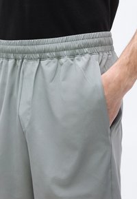 Άνδρας που φοράει ανοιχτό γκρι παντελόνι με ελαστική μέση και πλαϊνή τσέπη, με το δεξί χέρι εν μέρει μέσα στην τσέπη, με μαύρο πουκάμισο ορατό στη μέση.