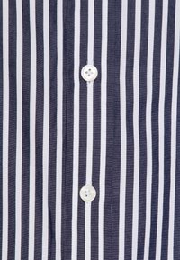 Navy and white striped shirt featuring a vertical pattern, light texture, and a central button closure with a four-hole button design.