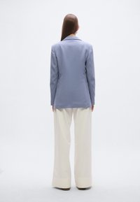 Ανοιχτό γαλάζιο blazer με εφαρμοστή γραμμή, που διαθέτει γιακά με σχισμή και μακριά μανίκια, συνδυασμένο με φαρδιά, κρεμ παντελόνια και καφέ παπούτσια.