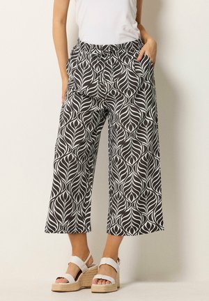 Vrouw draagt zwart-witte wijde cropped broek met bladmotief, met een gestrikte taille en witte platformsandalen.