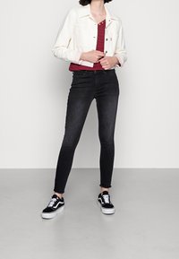 Vit denimjacka, röd randig överdel, svarta slim fit-jeans och svartvita Vans-skor. Har fransad nederkant på jeansen, avslappnad stil.