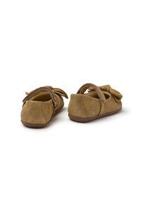 Zapatos infantiles de ante marrón con puntera redondeada, correa en la parte posterior y un lazo decorativo en el lateral. Suela blanda con un acabado texturizado.