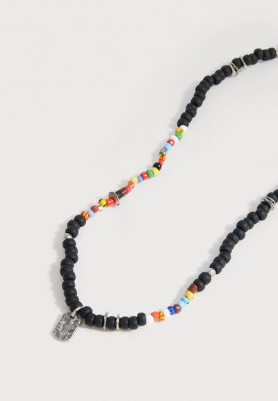 Κολιέ με χάντρες με μαύρες, πολύχρωμες χάντρες, ασημένια δαχτυλίδια και ένα μικρό ορθογώνιο ασημένιο μενταγιόν σε ανοιχτό φόντο.