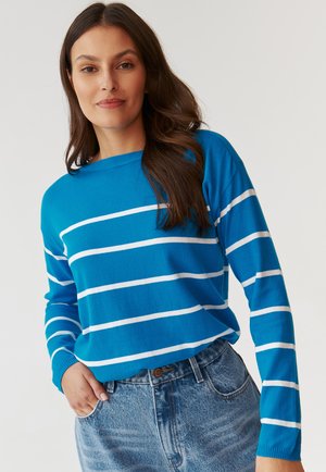 Pull bleu rayé avec des lignes blanches, encolure ronde, manches longues et texture douce. Associé à un short en denim taille haute.