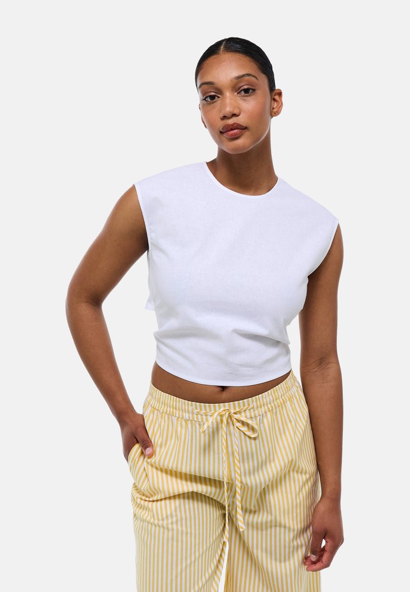 Top tank blanc court avec des manches courtes, doté d'un col rond, associé à un pantalon rayé jaune et blanc avec une taille à cordon.