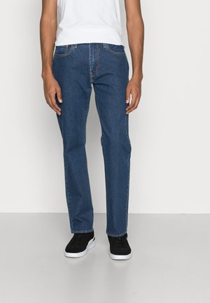 Jeans de mezclilla azul oscuro con corte recto, que cuentan con cinco bolsillos y costuras en contraste, combinados con zapatillas negras.