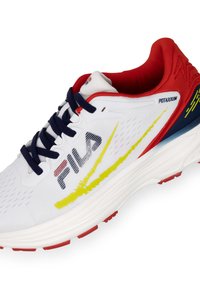 Witte sportieve schoen met rode en marineblauwe accenten, voorzien van een textuur bovenwerk, een opvallend "FILA"-logo en een gele swoosh ontwerpen.