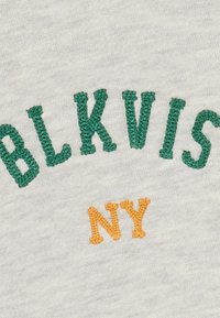 Šedá látka s vyšitým textom: „BLKVIS“ zelenou farbou a „NY“ oranžovou, s jemnou textúrou a neformálnym, zaobleným typom písma.